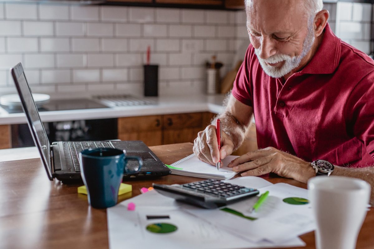 Senior man is sitting at table with laptop planning finances