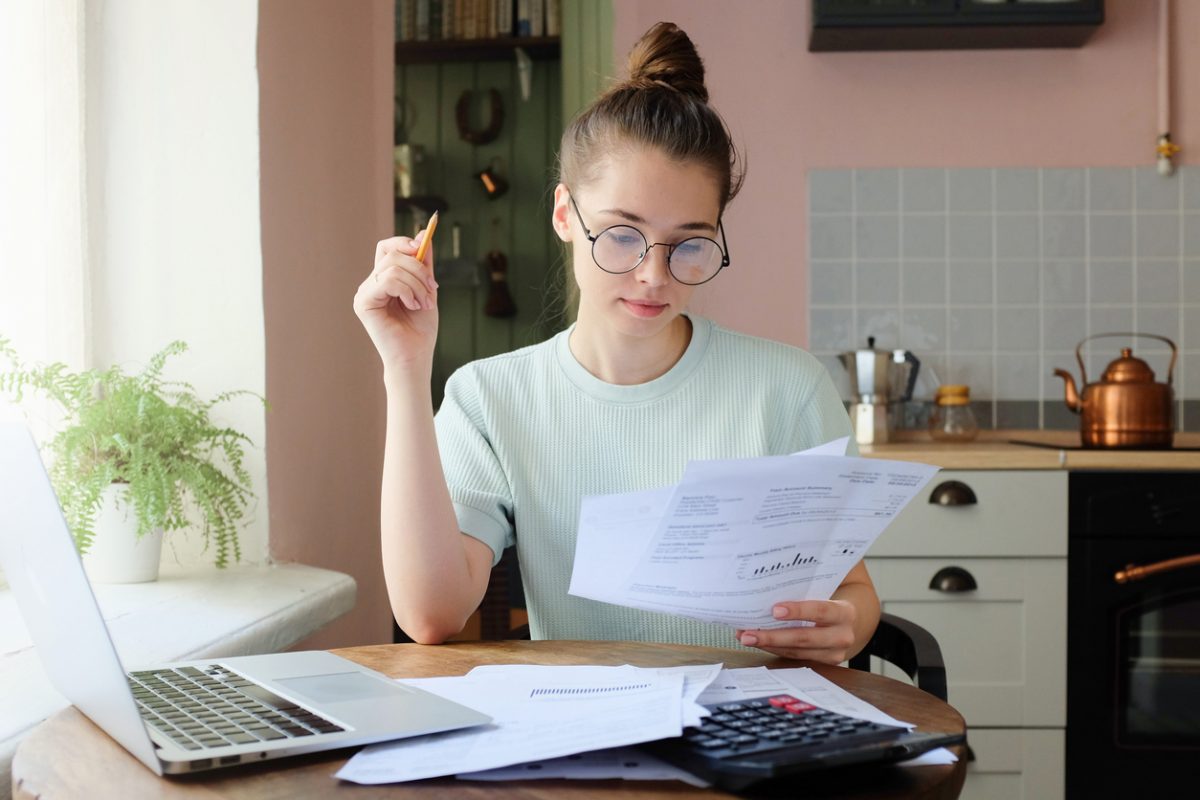 Young woman at a table with laptop and documents reviewing her finances
