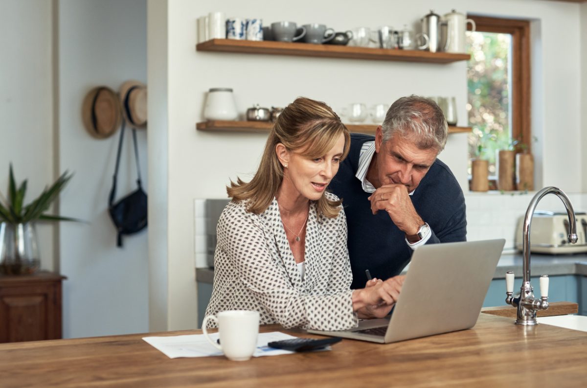 Mature couple in their kitchen reviewing finances on their laptop